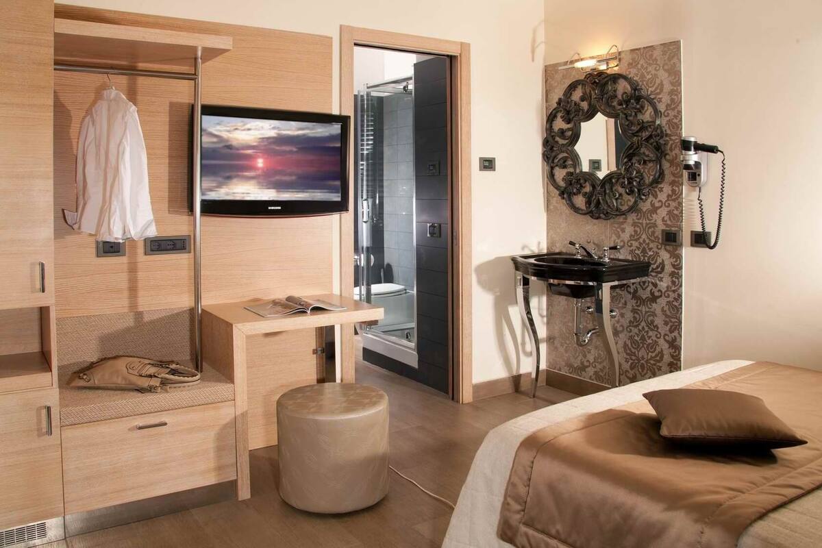 A modern hotel room with a bed, a desk, a TV, a bathroom, and a wardrobe.