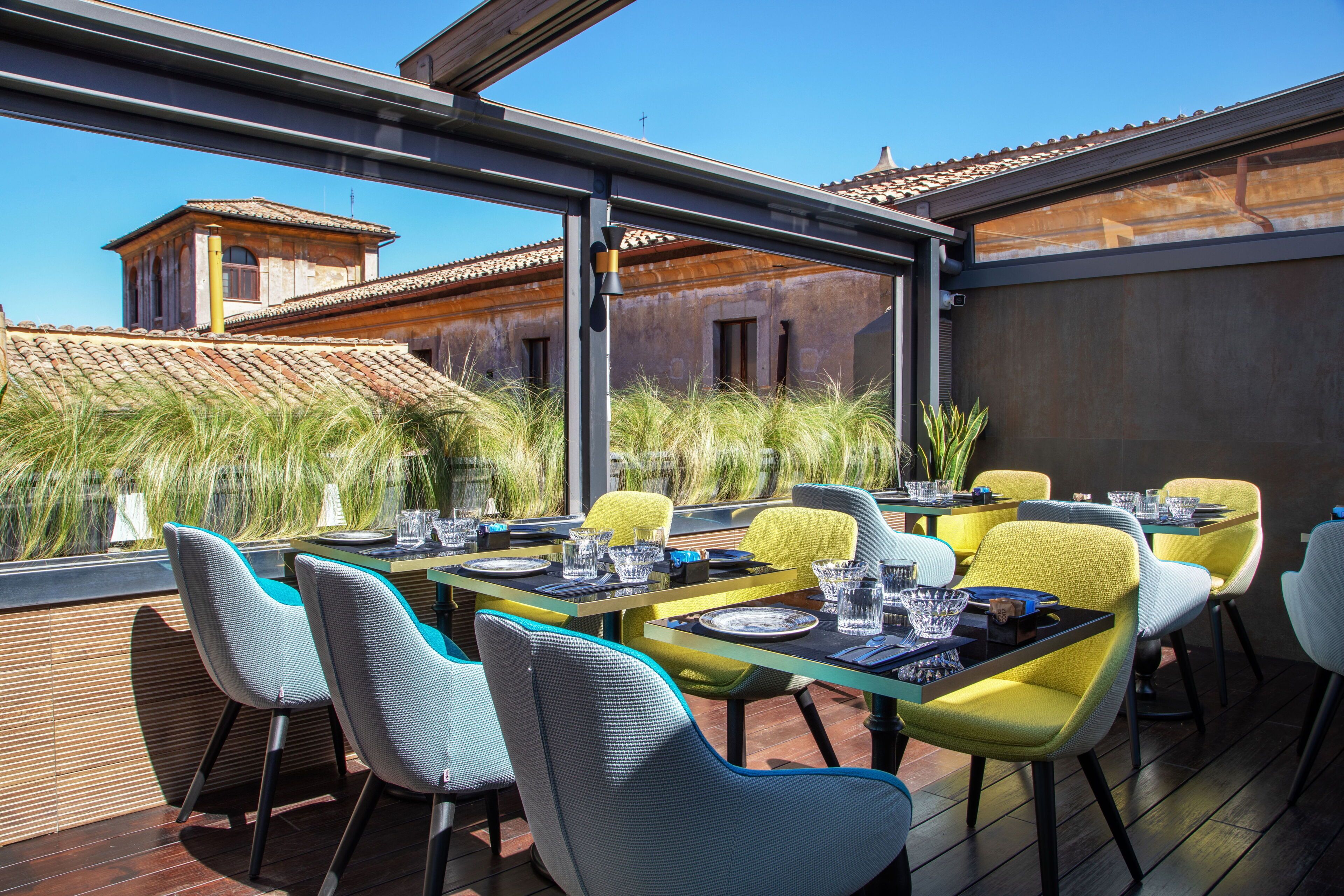 An outdoor dining area with tables and chairs, overlooking a building with a tiled roof.
