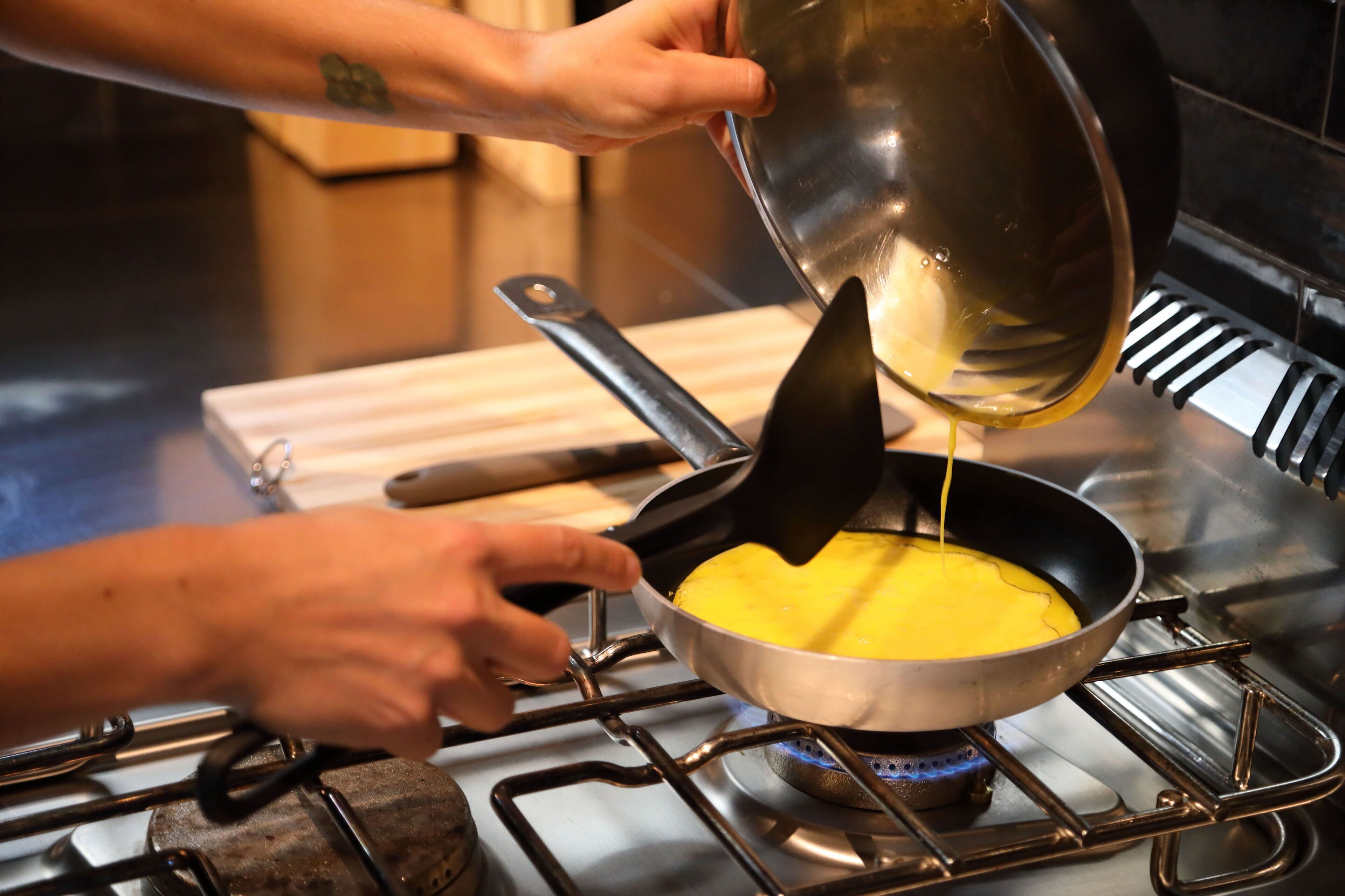 A person pouring a yellow liquid into a pan on a stove.