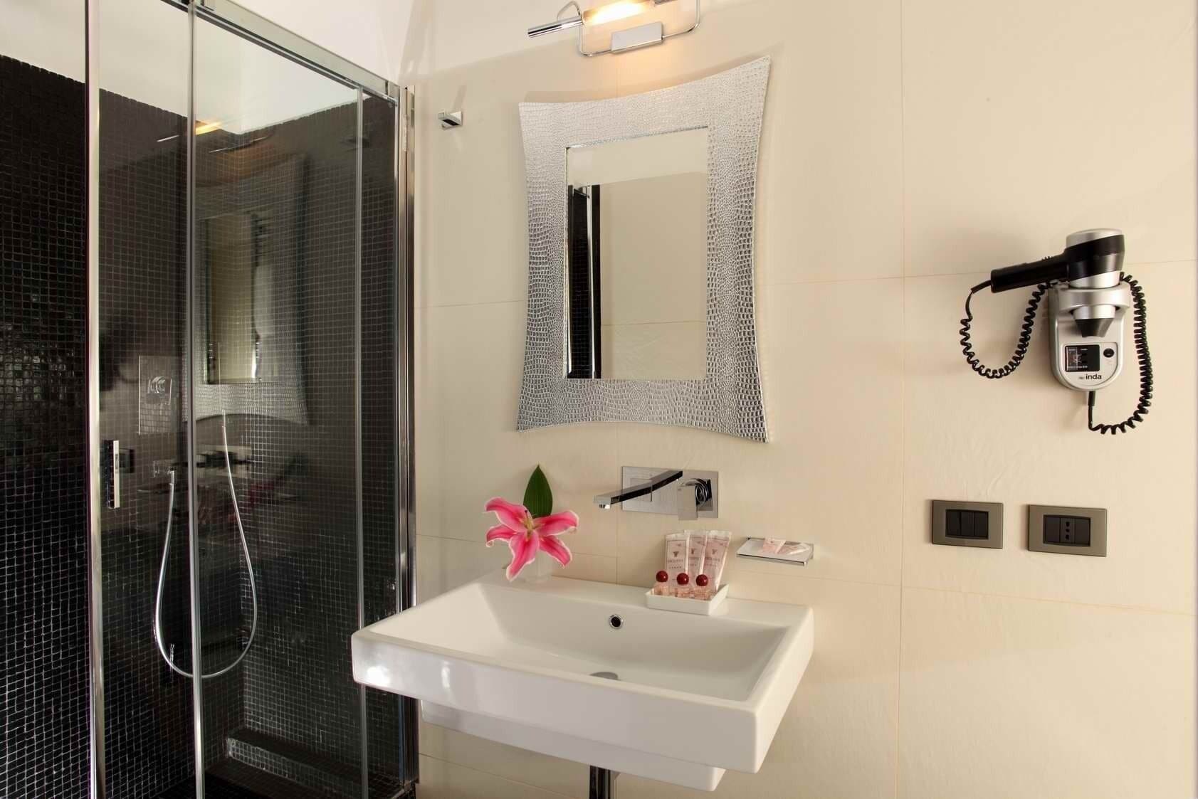 Une salle de bain avec une douche à parois de verre, un lavabo blanc, un miroir et un sèche-cheveux fixé au mur.