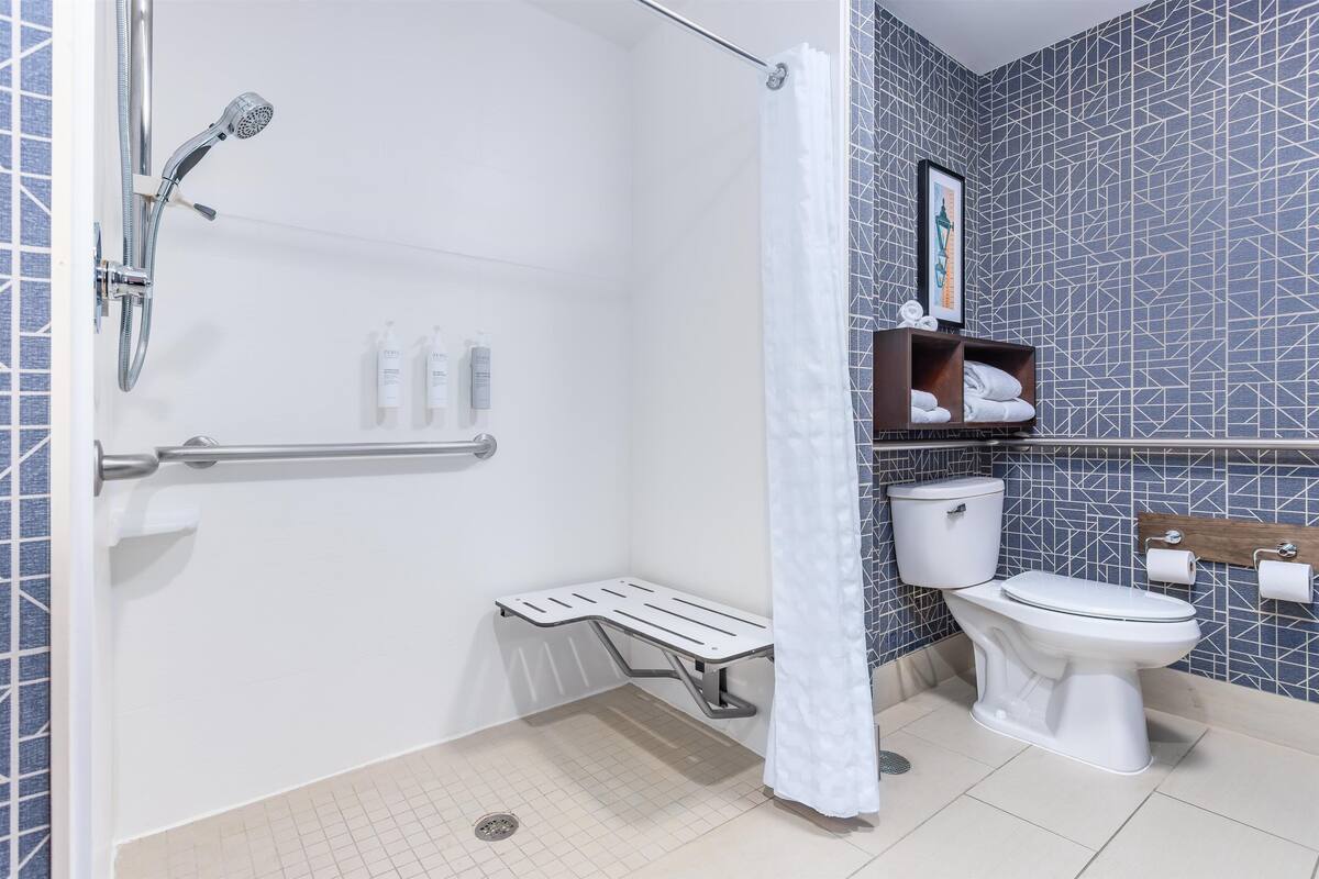Een badkamer met douche, toilet en een klein bankje.