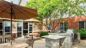 Un patio al aire libre con mesas y sillas de piedra, y una parrilla.
