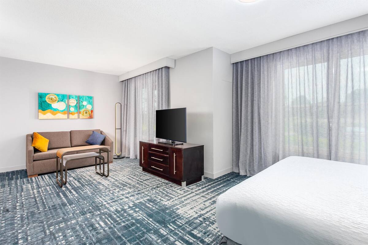 Een hotelkamer met een bed, een televisie, een bank, een salontafel en een schilderij aan de muur.