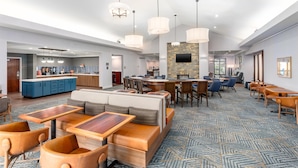Un moderno vestíbulo de hotel con una zona de bar, diferentes disposiciones de asientos y una cocina a la vista.