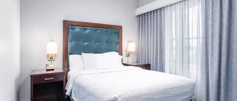 Ein Hotelzimmer mit einem großen Bett, zwei Nachttischen mit Lampen, einem Holzkopfende und einem Fenster mit Vorhängen.