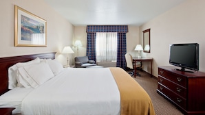 A hotel room with a large bed, a desk, a chair, a television, and a window with curtains.