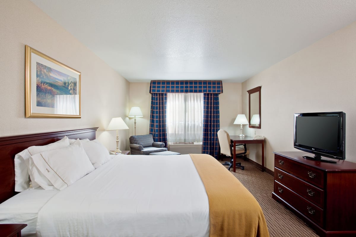 A hotel room with a large bed, a desk, a chair, a television, and a window with curtains.