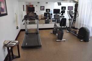 Sala de ginástica equipada com aparelhos de cardio, um espelho e um telefone sobre uma mesa.