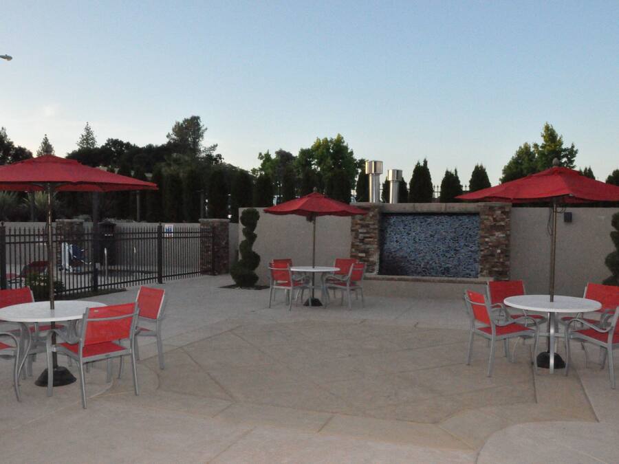 An outdoor patio area with tables and chairs, red umbrellas, and a decorative wall.
