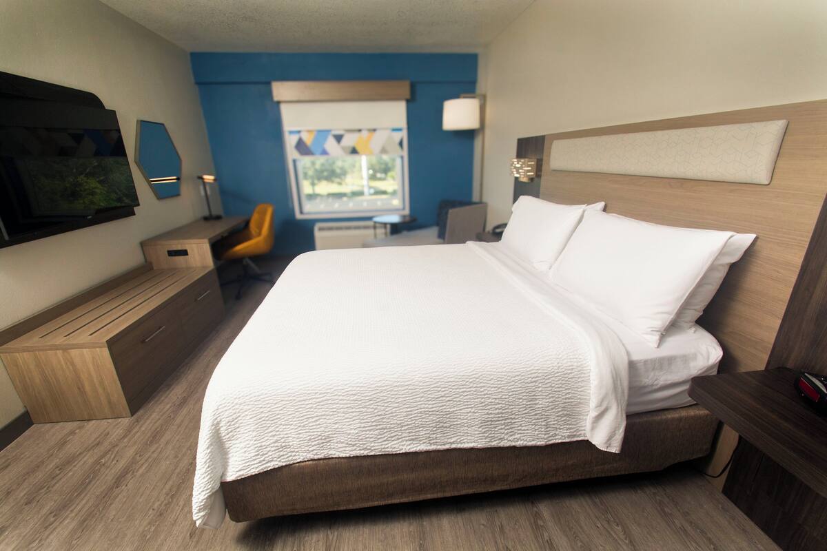 Une chambre d’hôtel avec un grand lit, un bureau avec une chaise, une télévision et une fenêtre donnant sur un beau paysage.