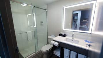 A bathroom with a glass-enclosed shower, a toilet, a sink with a mirror, and a towel rack.