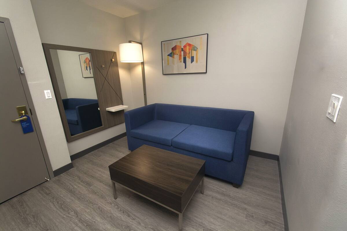Une pièce avec un canapé bleu, une table basse en bois, un miroir et une lampe fixée au mur.