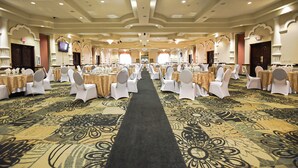 A banquet hall with rows of tables and chairs, a carpeted floor, and chandeliers.