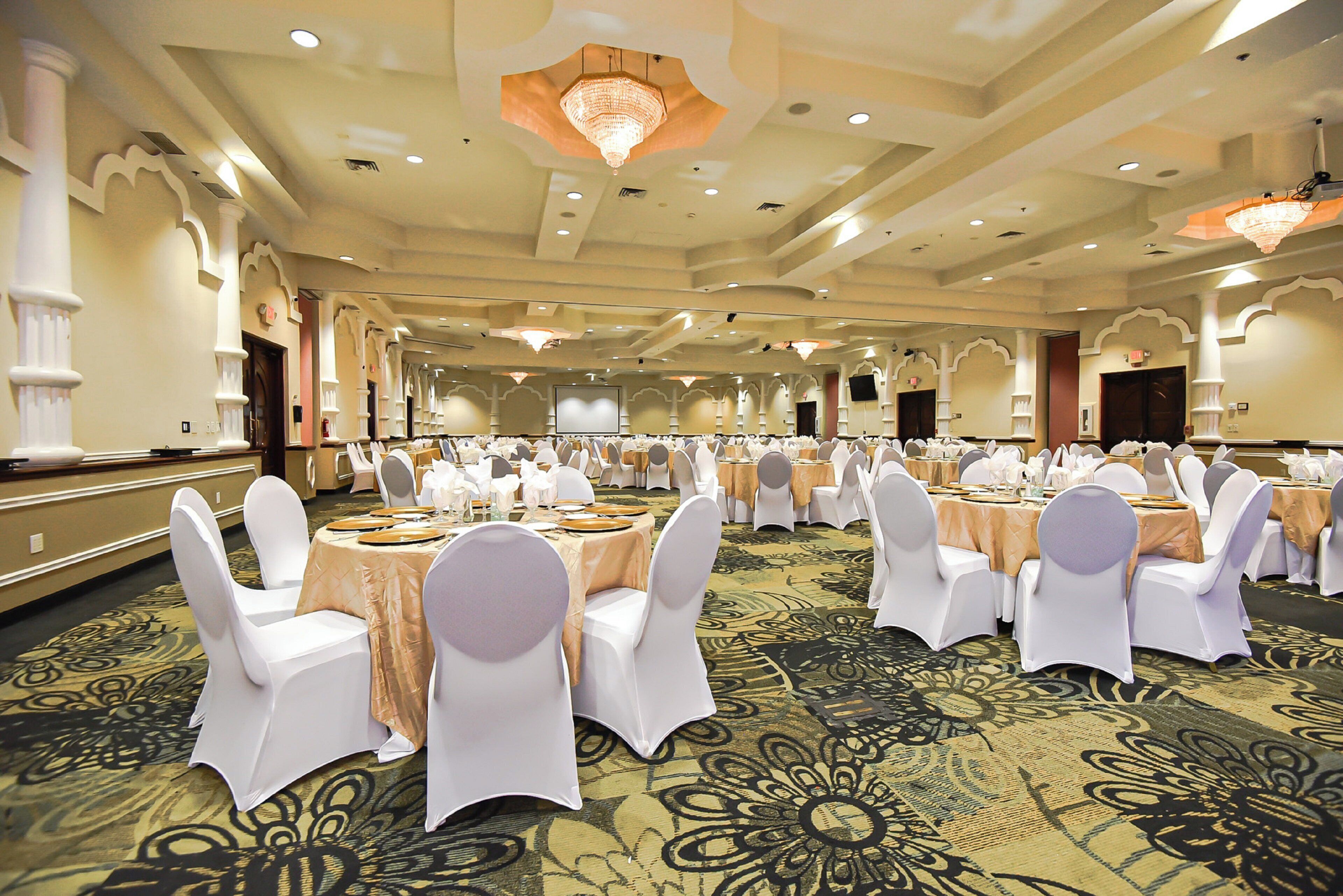 A banquet hall with round tables, white chairs, and chandeliers.