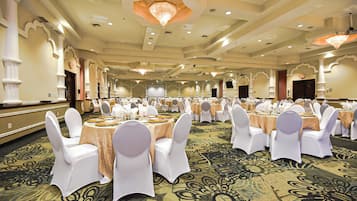 A banquet hall with round tables, white chairs, and chandeliers.
