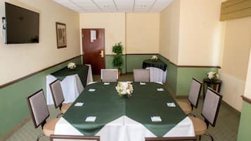 A conference room with a green table, white chairs, a TV on the wall, and a door in the background.