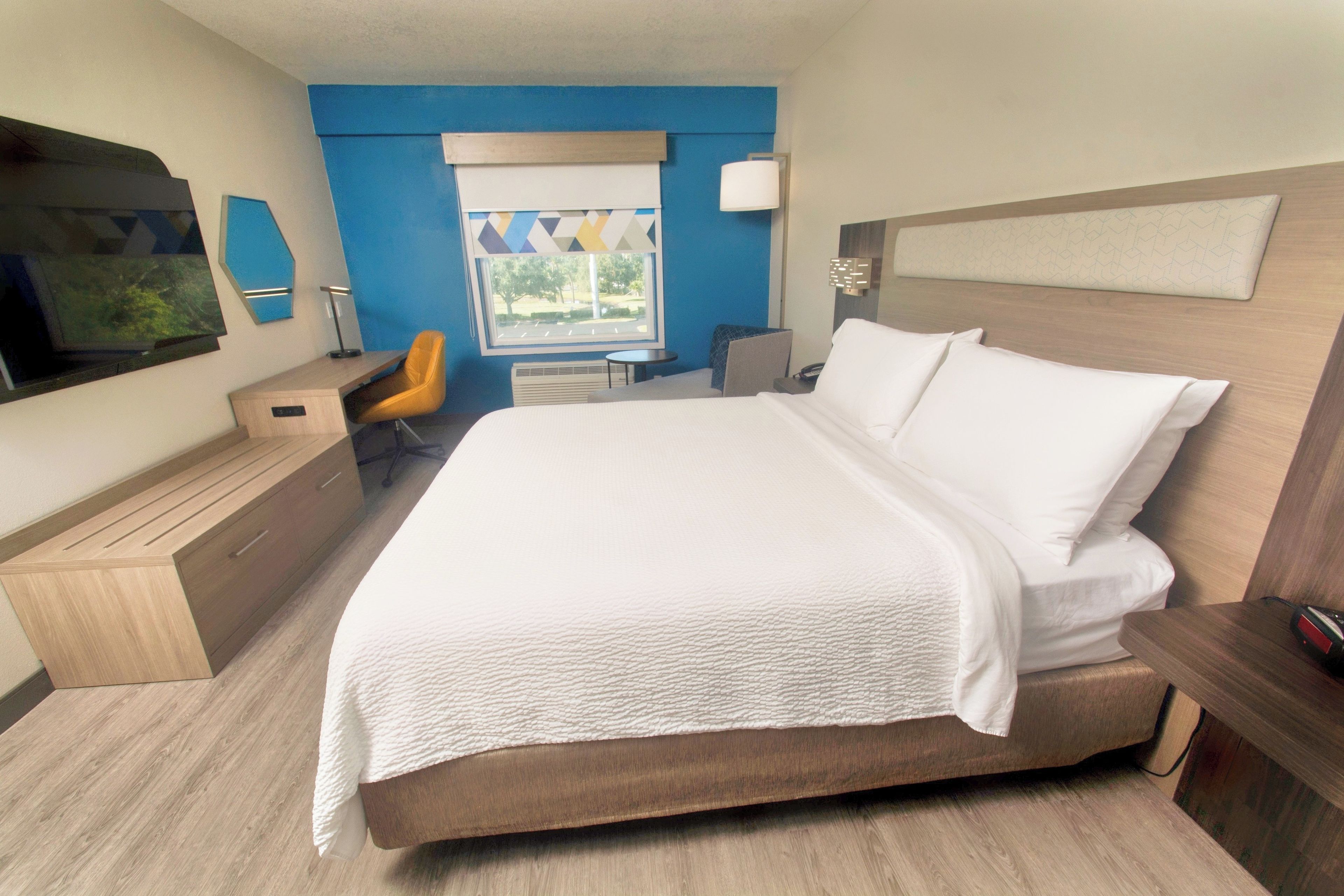 A hotel room with a large bed, a desk, a chair, a TV, and a window with a view of the outdoors.