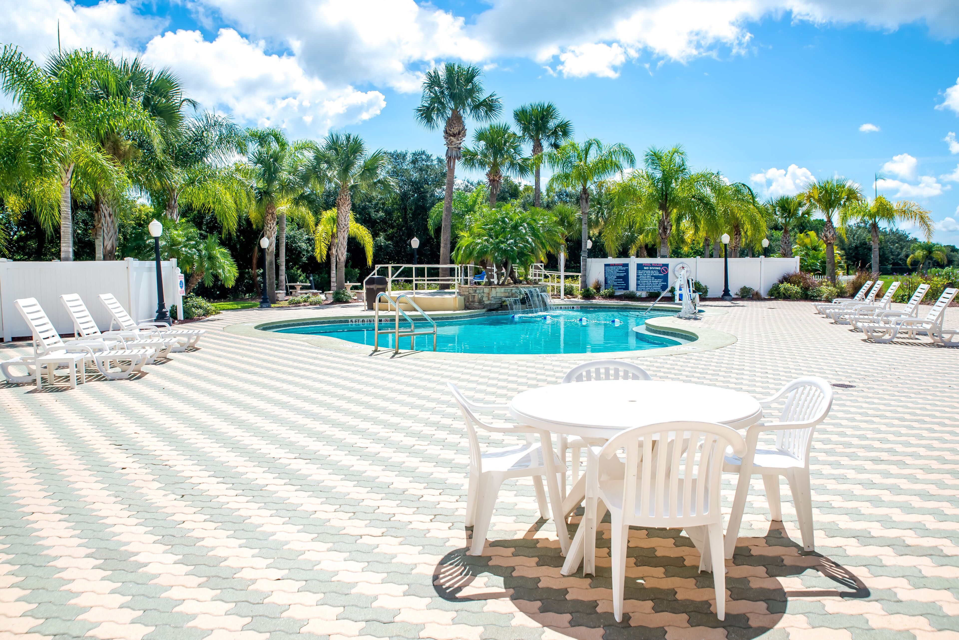 A pool area with a circular pool, white lounge chairs, and palm trees.