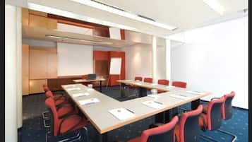 A conference room with a long table, red chairs, a whiteboard, and a projector screen.
