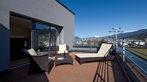 Un balcón con muebles de mimbre, una botella de vino y vistas a la ciudad y montañas.