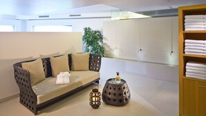 Un baño moderno con sofá, cabina de ducha de vidrio, estante de madera con toallas y una planta en maceta.