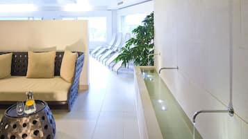 Relax in a stylish space with a sofa, ottoman, and bathtub, surrounded by lush greenery.