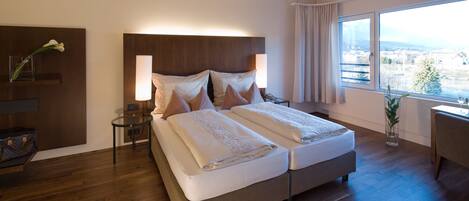 A double bed with a wooden headboard, bedside tables, a desk, and a large window with a city view.