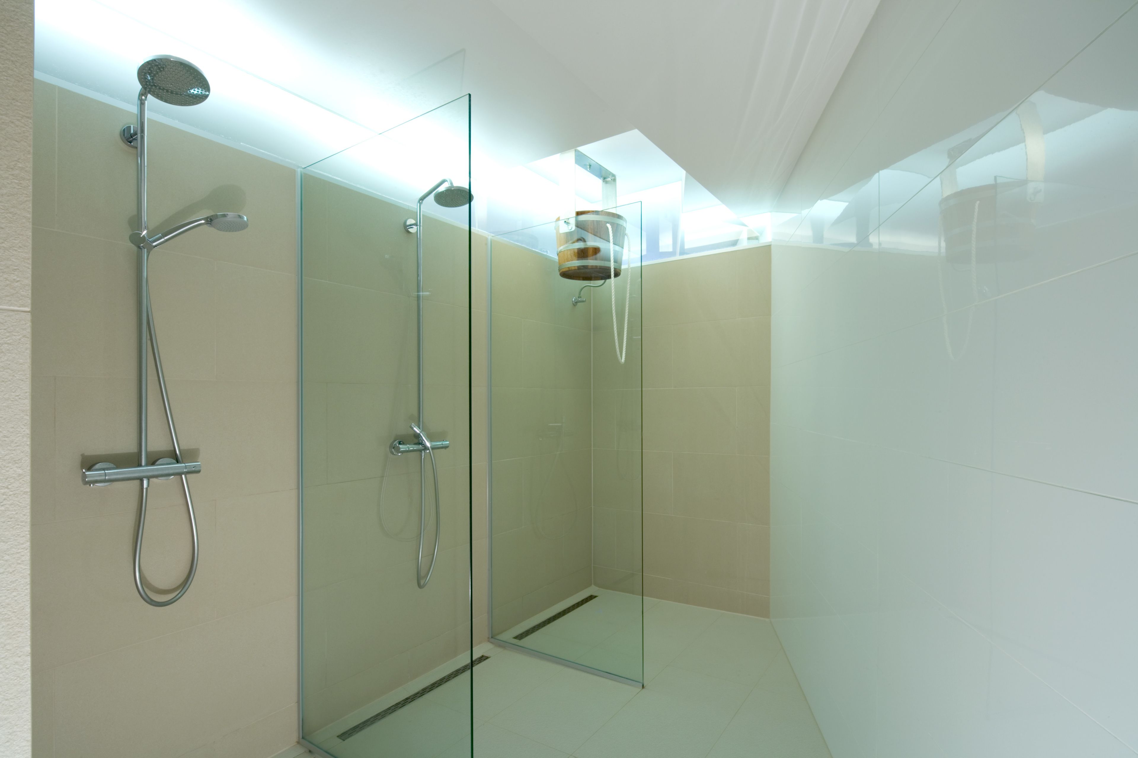 Ein modernes Badezimmer mit einer Glaskabine zur Dusche, einer Handbrause und einem am Wand montierten Wasserhahn.