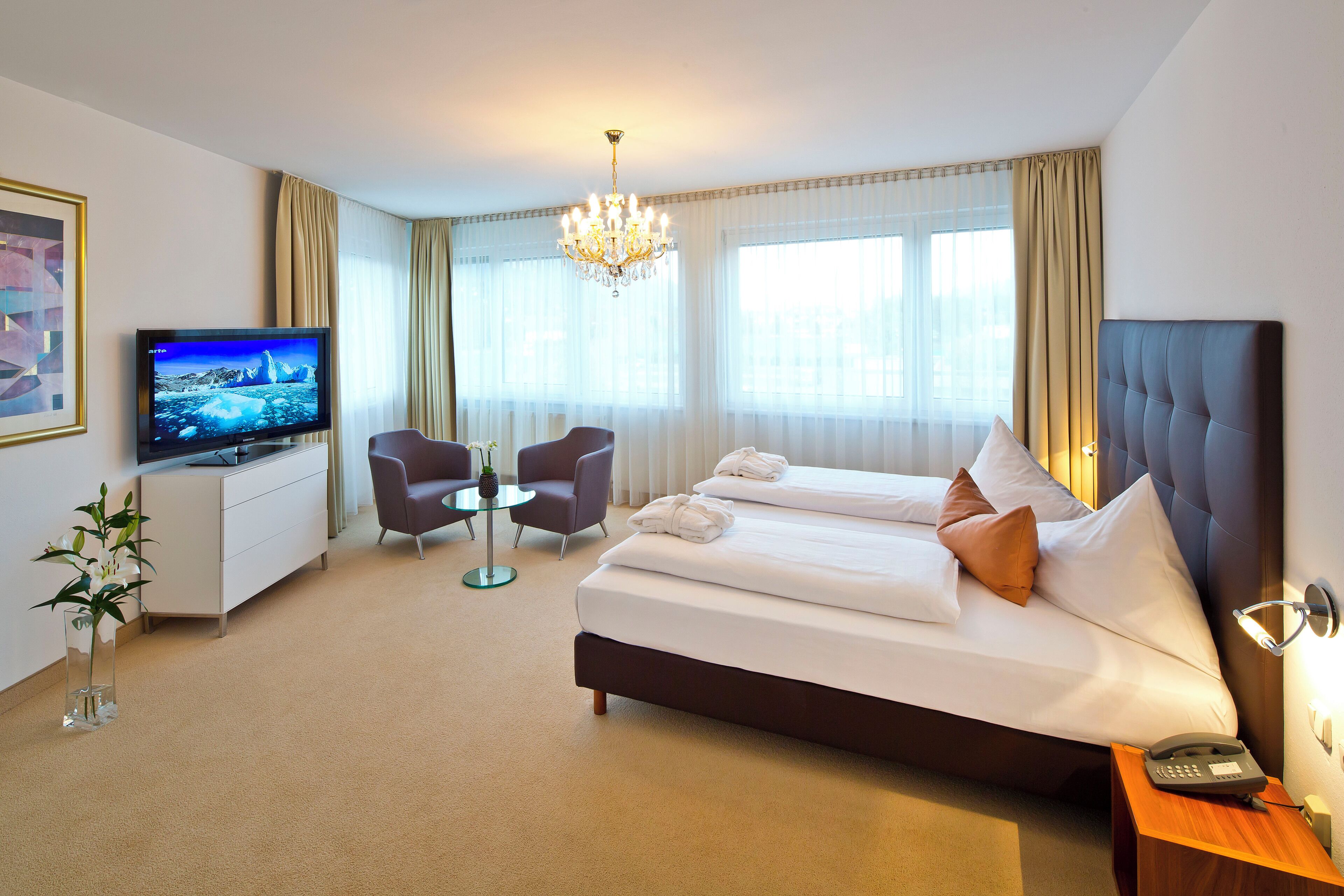 Ein Hotelzimmer mit Bett, Fernseher, Schreibtisch, Stuhl und einer Pflanze.