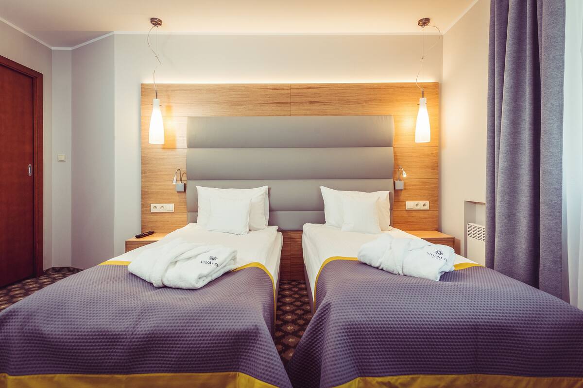 Habitación de hotel con dos camas, cabecera de madera, lámparas de noche y mesita con control remoto.