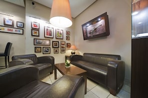 A room with a brown leather sofa, a wooden coffee table, and a wall adorned with framed pictures. - Vivaldi Hotel (Poznan)