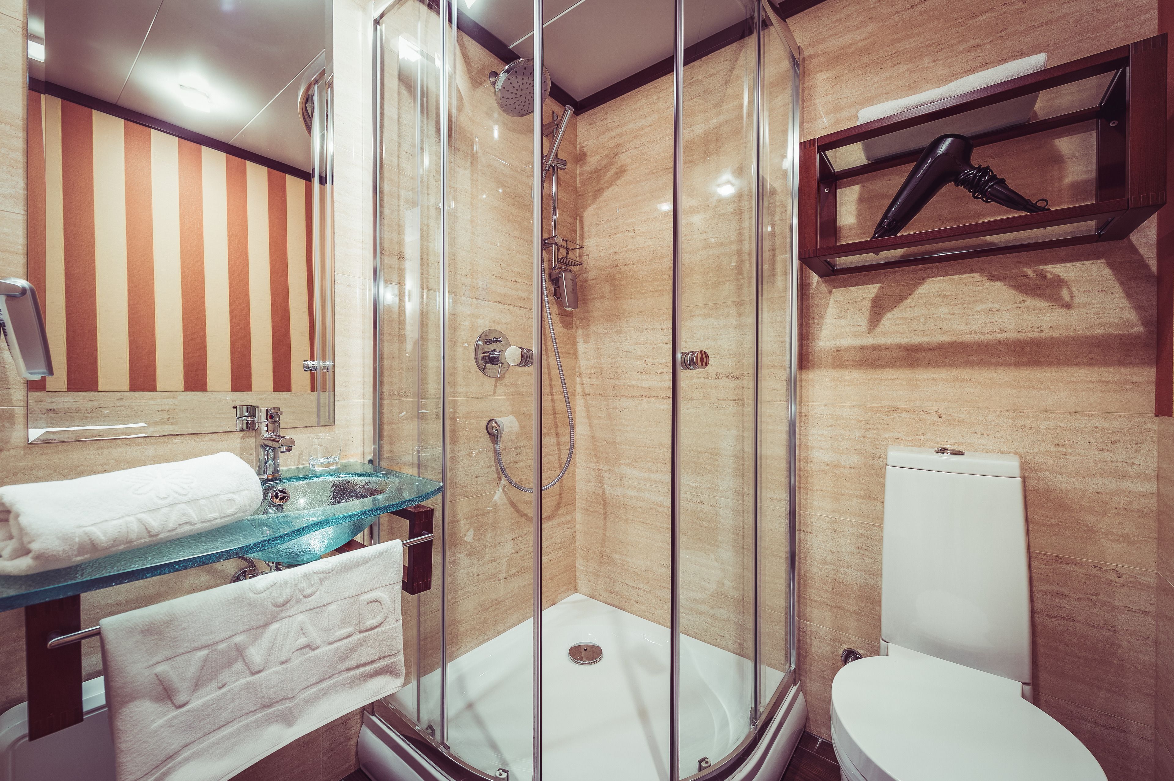 A bathroom with a glass shower enclosure, a white toilet, and a glass sink with a towel rack.