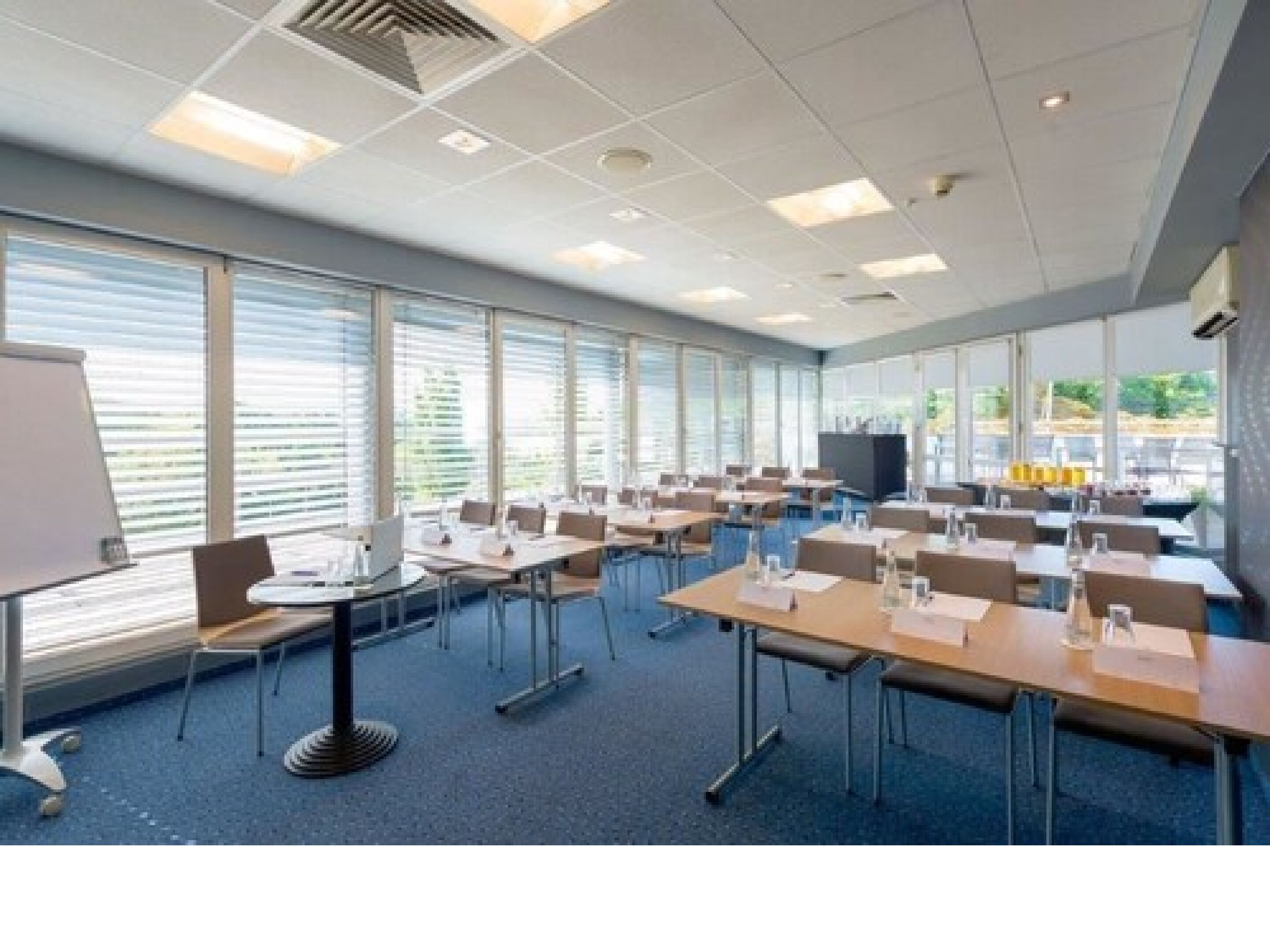 A conference room with tables and chairs, large windows, and a whiteboard.