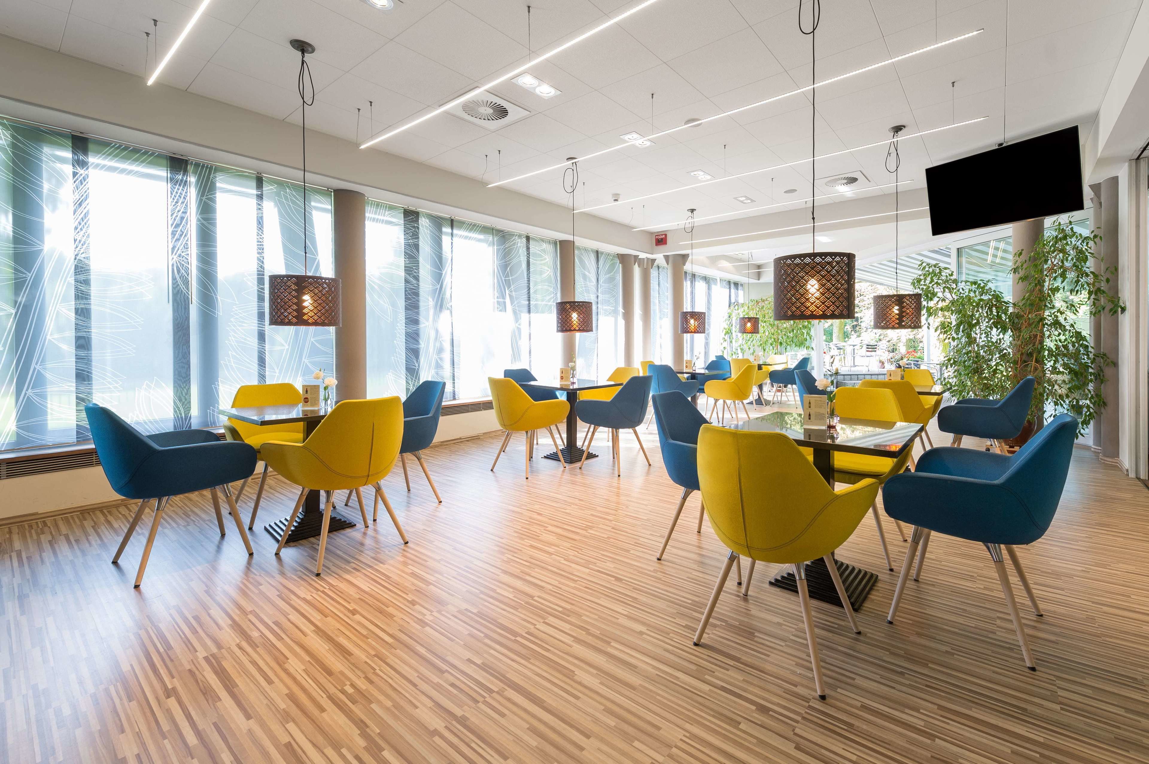 Ein moderner Konferenzraum mit Holzboden, gelben und blauen Stühlen und hängenden Pendelleuchten.