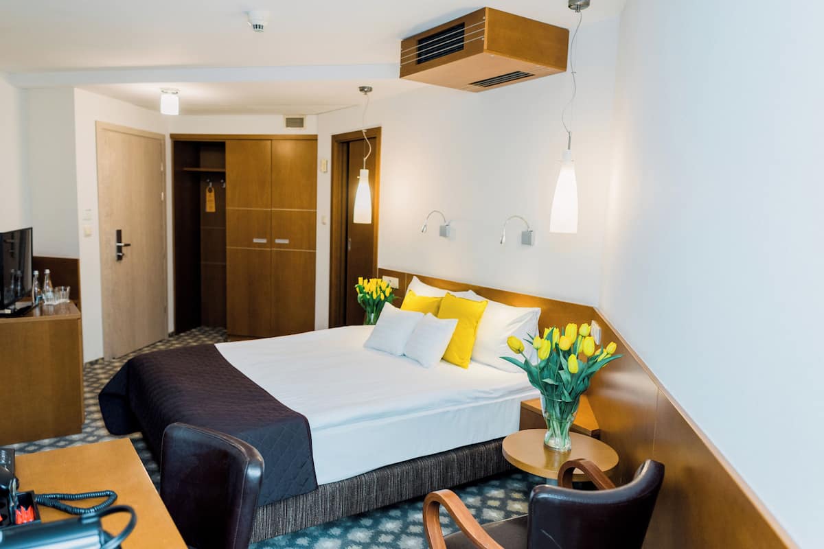 Una habitación de hotel con cama, mesita de noche, silla y escritorio con teléfono.