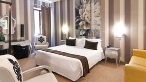 Habitació d'hotel amb un llit gran, una taula de nit, una cadira, un escriptori, un mirall i una obra d'art floral de grans dimensions a la paret.