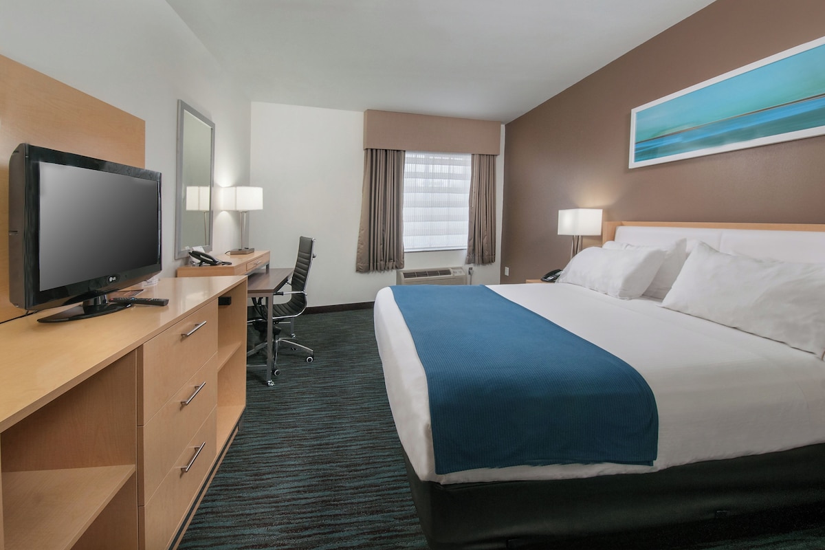 Una habitación de hotel con una cama, un escritorio con televisor, una silla y una ventana con cortinas.