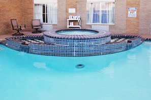 Une piscine avec un jacuzzi, des marches carrelées et une chaise.