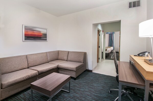 Habitación de hotel moderna con sofá modular, una mesita, un escritorio con lámpara y un cuadro en la pared.