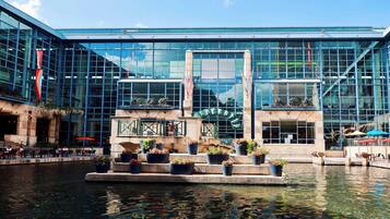 A modern building with a glass facade, a water feature in front, and outdoor seating areas.