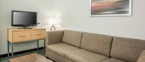 A hotel room with a sofa, a television on a wooden cabinet, a lamp, and a framed picture on the wall.