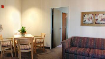A hotel room with a dining area featuring a table and four chairs, a sofa, and a framed picture on the wall.