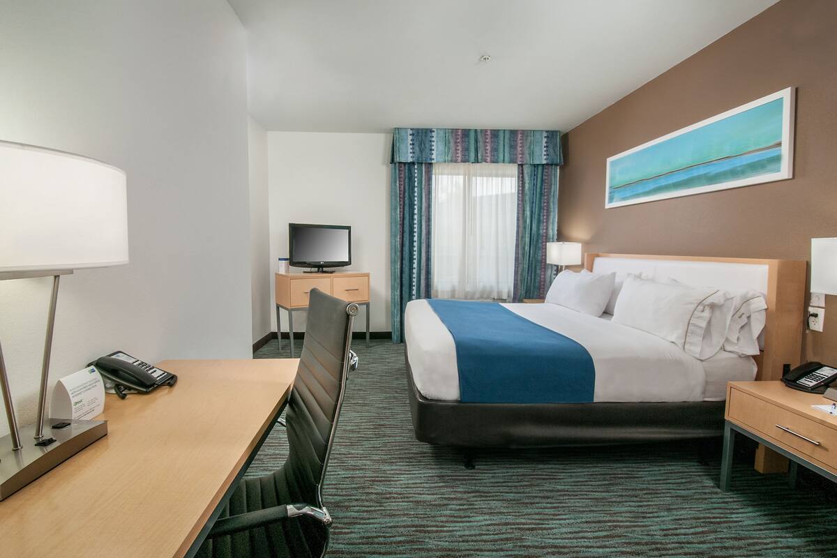 A hotel room with a bed, desk, chair, television, and a painting on the wall.