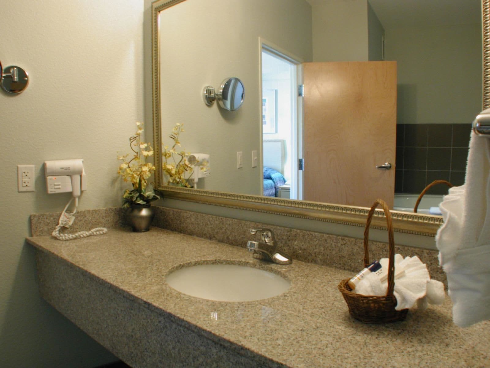 A bathroom with a granite countertop, a sink, a mirror, a hairdryer, and a basket with towels.