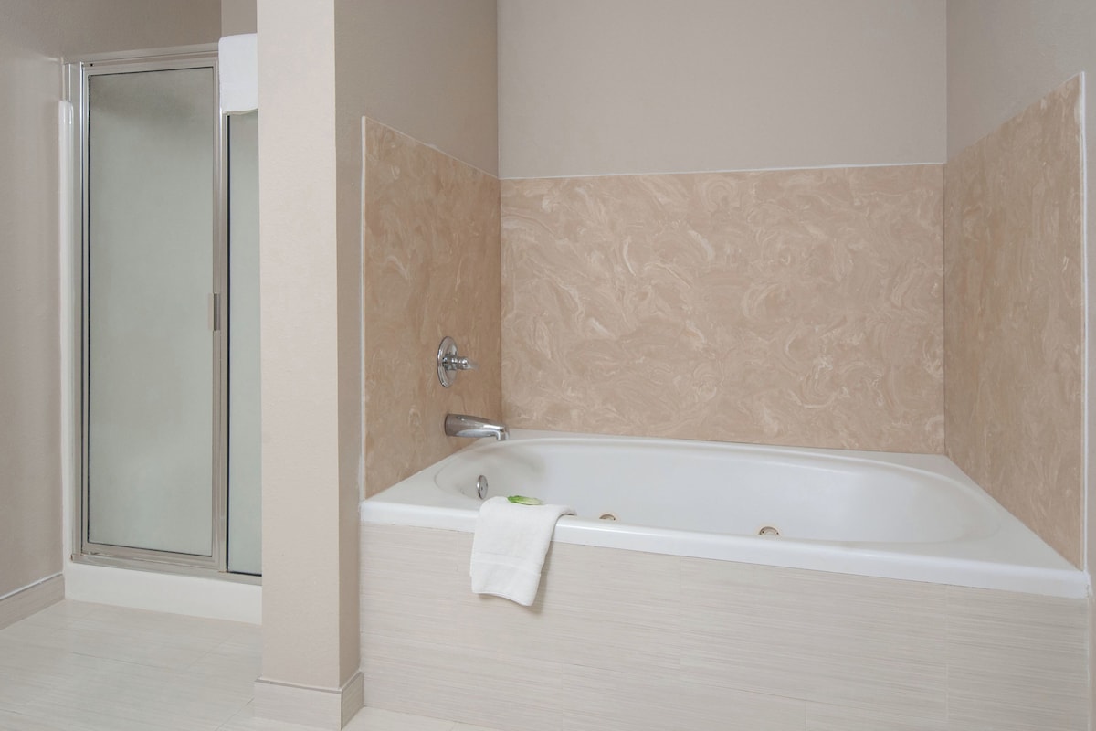 Un baño con cabina de ducha de vidrio, bañera y paredes de mármol color crema.