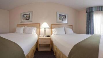 A hotel room with two single beds, a nightstand with a lamp, and two framed pictures on the wall.
