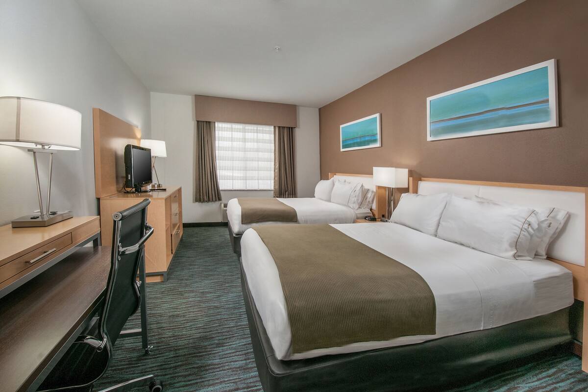 A hotel room with two beds, a desk, a chair, a television, and two paintings on the walls.