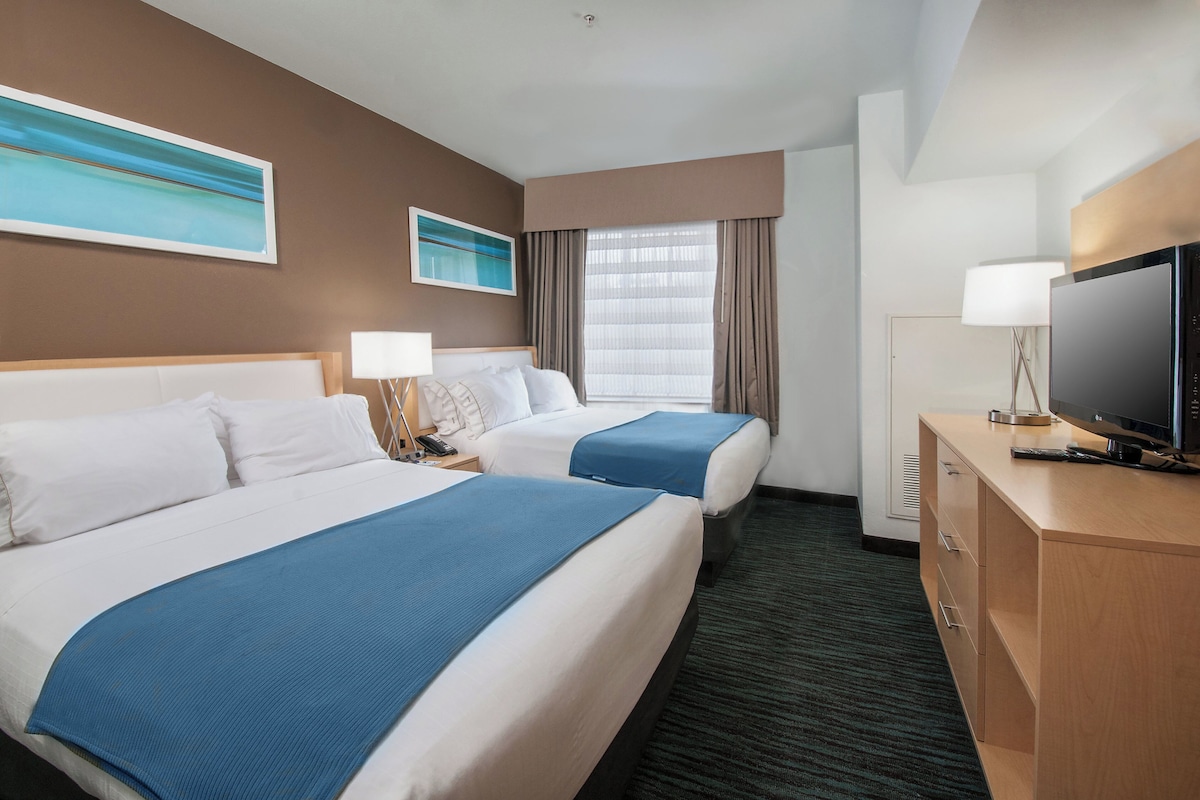 Habitación de hotel con dos camas, televisión, escritorio y ventana con cortinas.