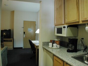 Una cocina compacta equipada con microondas, cafetera y un pequeño comedor con una silla y una mesa.