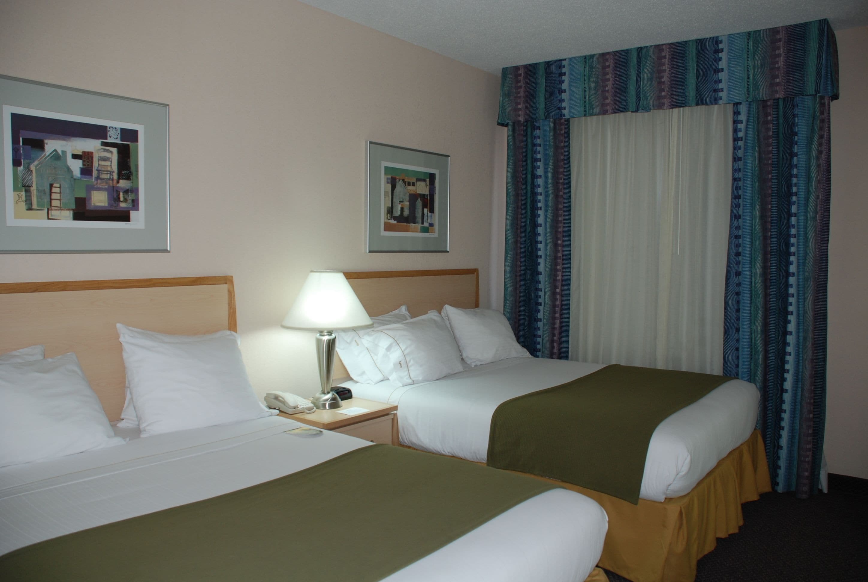 Ein Hotelzimmer mit zwei Betten, einem Nachttisch mit Lampe und zwei gerahmten Bildern an der Wand.